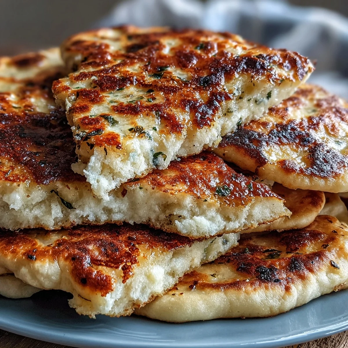 Stack of fluffy The Best Easy Garlic Naan Bread served beside a bowl of creamy curry.