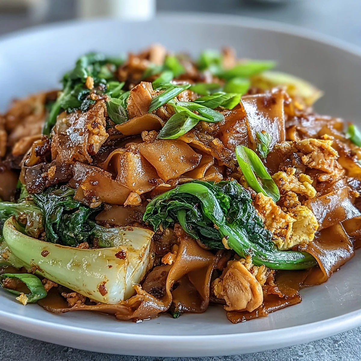 Golden-brown Authentic Thai Pad See Ew noodles glisten in a wok, tossed with tender chicken, vibrant Chinese broccoli, and a savory-sweet sauce.  