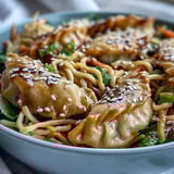Golden lo mein noodles and vegetable potstickers glisten in a hot skillet, tossed with bright carrots and cabbage.