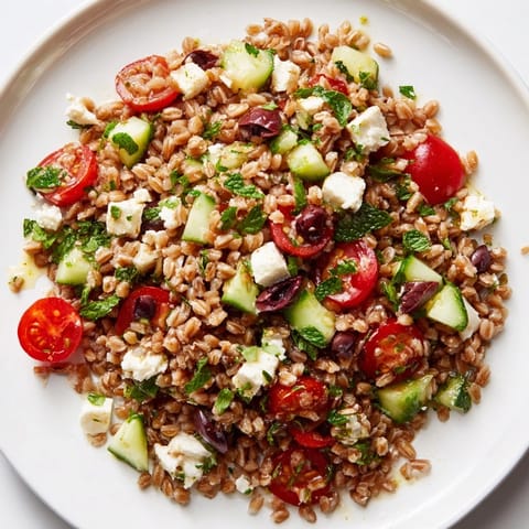 Hearty farro Mediterranean salad features cherry tomatoes, cucumbers, red onion, olives, and feta, drizzled with zesty lemon dressing for a refreshing side.