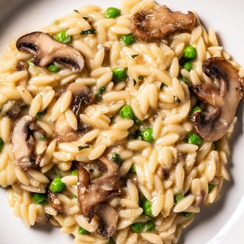 A steaming bowl of Orzo Mushroom Risotto-Style with sautéed mushrooms and green peas, served on a rustic wooden table.  