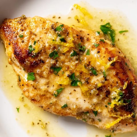 A close-up of Lemon Pepper Chicken with vibrant lemon zest, cracked pepper, and a rich sauce pooling.