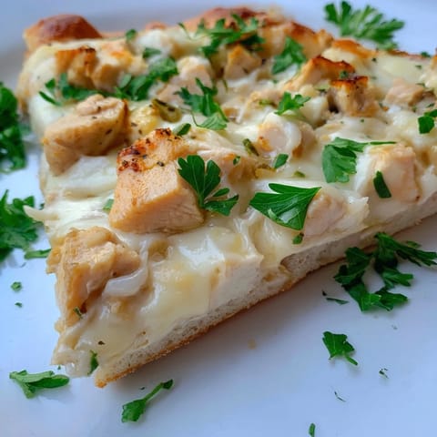 Slices of Chicken Alfredo Pizza display bubbly mozzarella, savory chicken, and a rich white sauce on a wooden board.