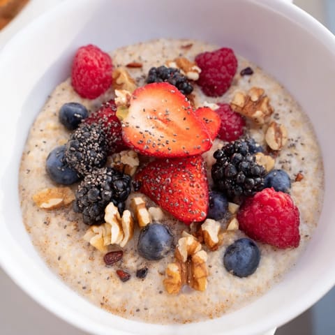Creamy, golden Millet Porridge With Berries steams gently, featuring a hint of cinnamon and nutmeg for a cozy, nourishing breakfast.