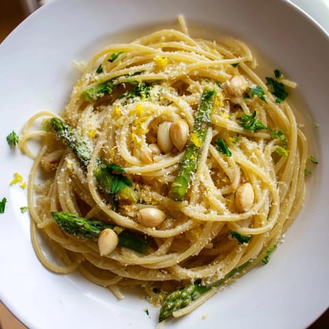 A close-up of Roasted Garlic & Asparagus Pasta shows tender spears and mashed garlic in a glossy, herb-flecked sauce.  