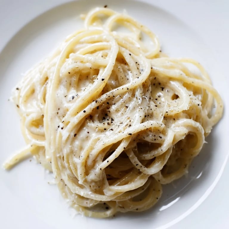 Close-up of al dente spaghetti cacio e pepe, glistening with melted cheese and fragrant black pepper flakes.  