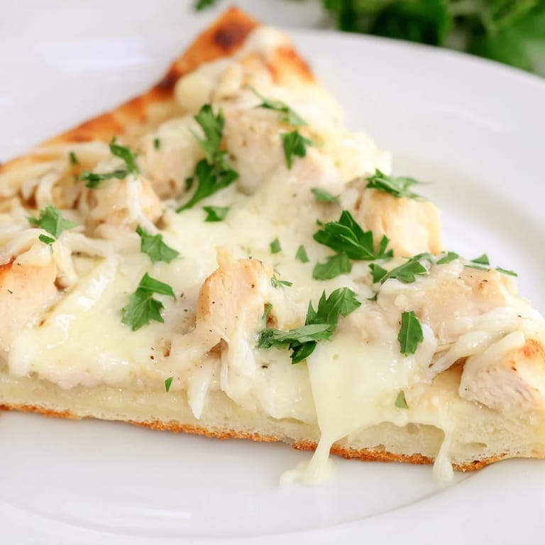 A close-up of Chicken Alfredo Pizza reveals a crispy edge, fresh parsley garnish, and a cheesy, indulgent topping.