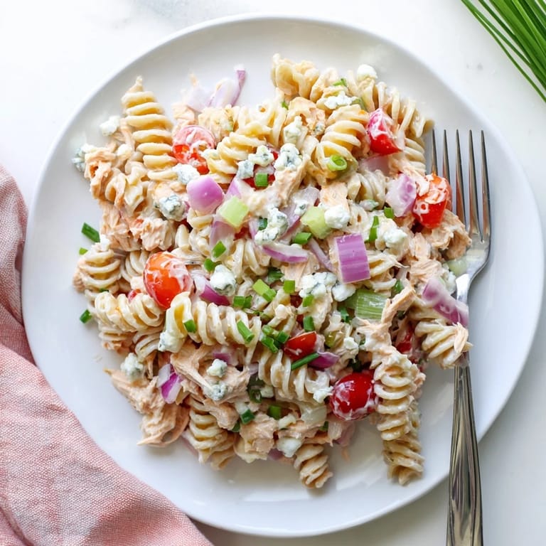 A hearty bowl of Buffalo Chicken Pasta Salad featuring blue cheese crumbles and fresh chives, perfect for a summer potluck or picnic.